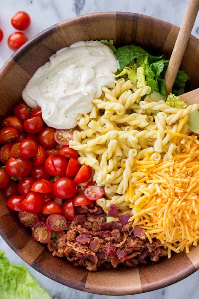 BLT pasta salad showing halved cherry tomatoes, mayo based dressing, chopped romaine, cheddar cheese, pasta, and real bacon pieces. 