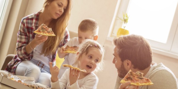 Mom, dad, 6 year old boy and 4 year old girl eating Aldi pizza in the living room as part of their Aldi Meal Plan that delivers 14 meals to their front door that can be made in under 15 minutes for under $150. 