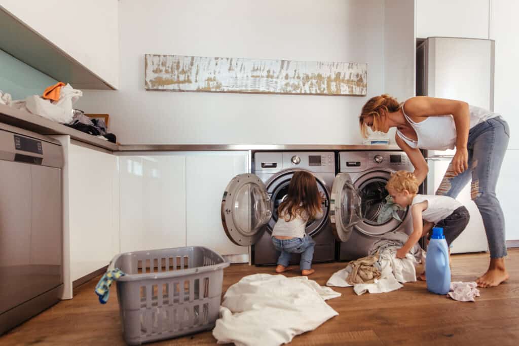 Mother teaching kids to load clothes in washing machine. 