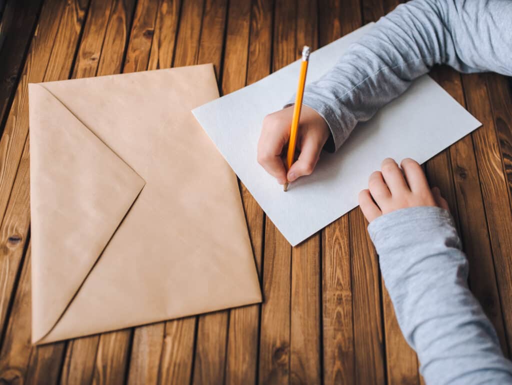 Children's hands write a letter. A brown envelope, a white sheet of paper and a pencil.