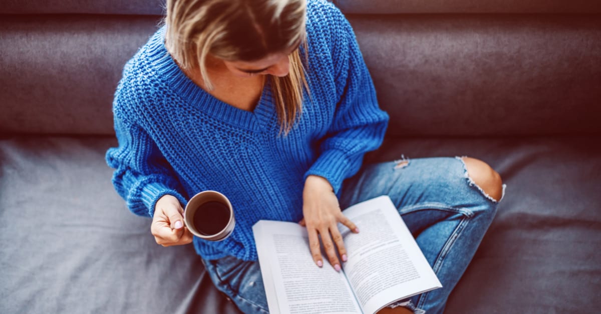 Young woman sitting on the couach with a cup of cofee reading.