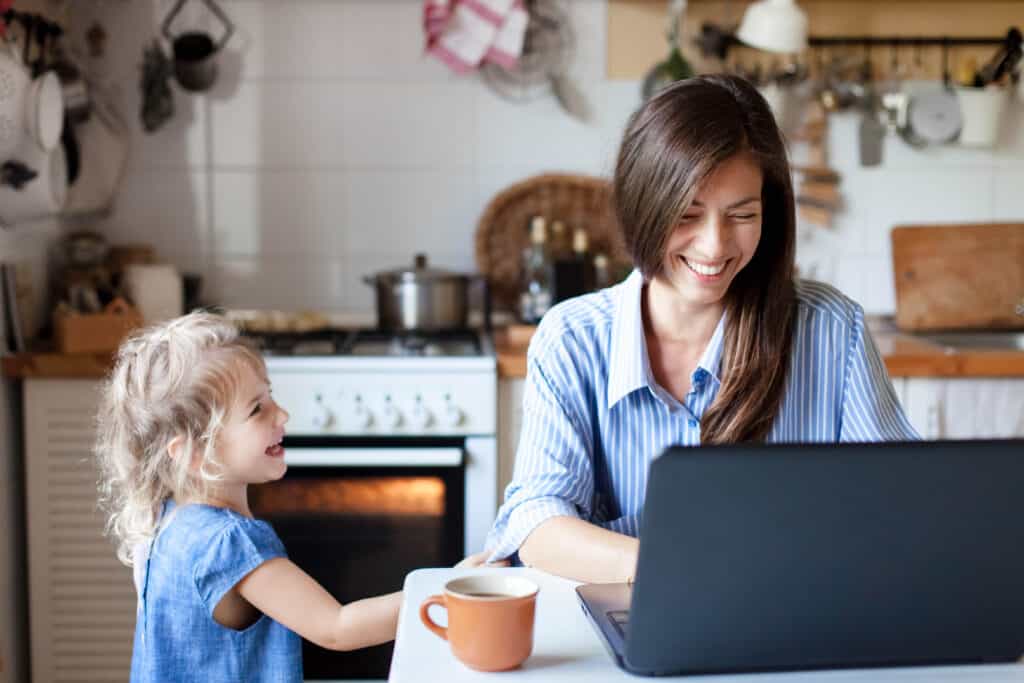 Mom working from home with daughter sitting at the kitchen table.
