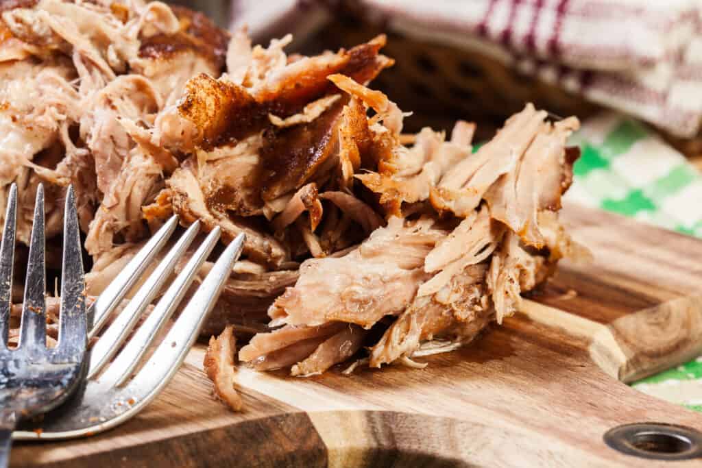 Slow cooked pulled pork shoulder on chopping board with forks