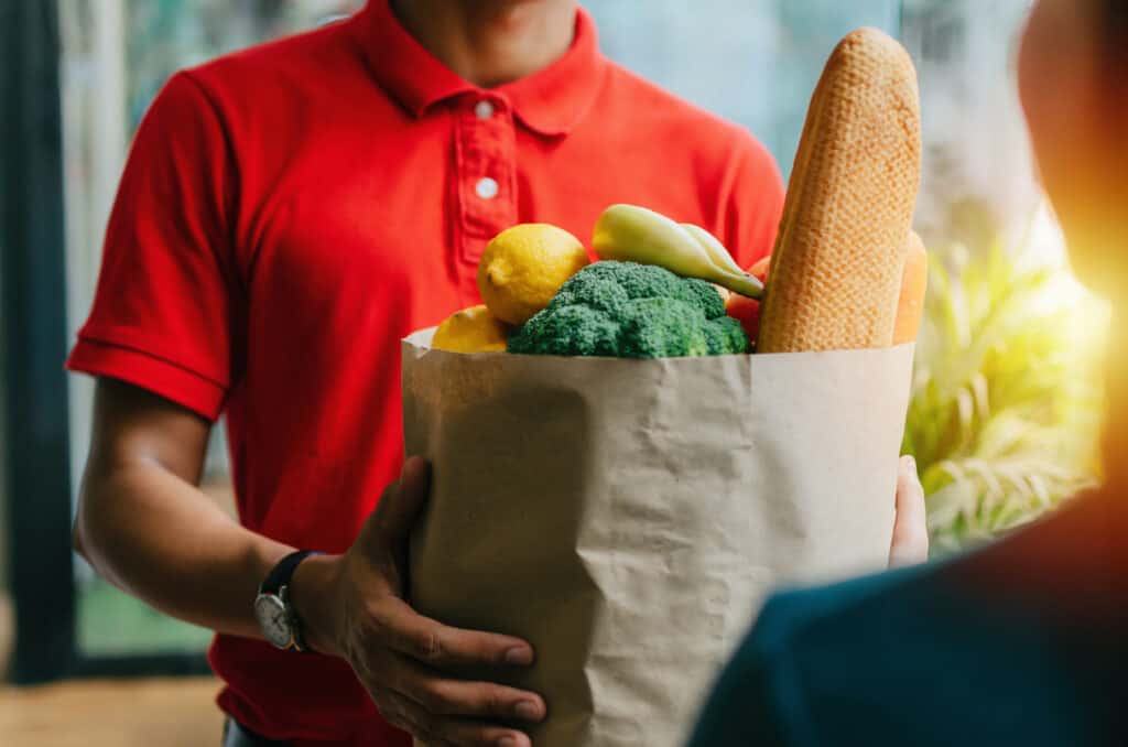 Man in red shirt delivering a bag of groceries.