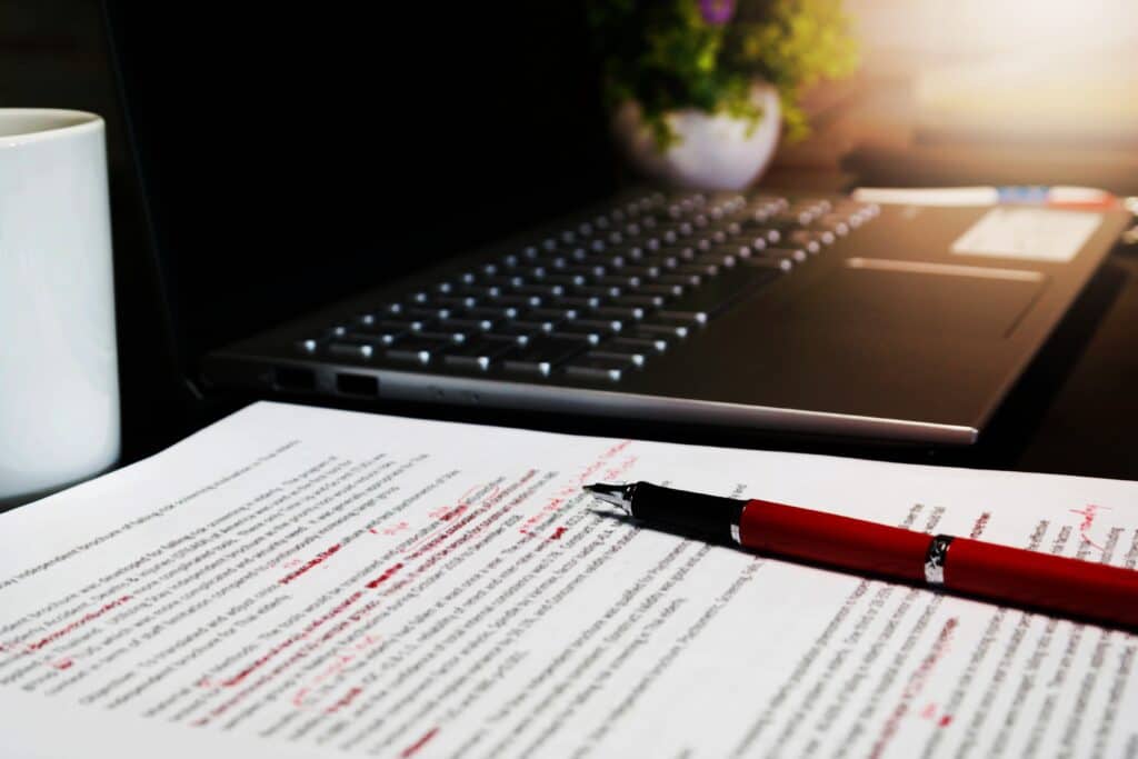 blur proofreading sheet on table with red pen and laptop